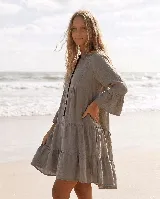 Vestido corto de lino natural color gris, con diseño amplio de capas, escote en V con botones frontales y mangas largas con volados en los puños.