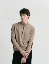 Sweater de punto color verde oliva, con cuello alto y medio cierre frontal. Presenta coderas en símil nappa y puños acanalados.