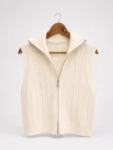 Chaleco de punto trenzado color crema, con cuello alto y cierre frontal completo. Presenta terminaciones en tejido acanalado en sisas y ruedo.