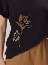 Remera negra de manga corta con cuello redondo y detalle de bordado floral en tono tostado en la parte inferior derecha.