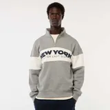 Buzo gris con cuello alto y cremallera parcial, con franja blanca horizontal en el pecho con la inscripción "New York Upper East Side" en azul marino.