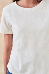 Remera de algodón color blanco con bordados florales y geométricos en color negro. Presenta cuello redondo, mangas cortas y un diseño con franjas horizontales bordadas.