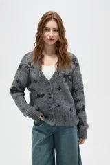 Cardigan de punto gris con estampado de estrellas negras, cuello en V, cierre frontal con botones y mangas largas con puños acanalados.
