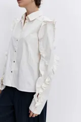 Camisa de color azul oscuro, con cuello clásico, cierre frontal de botones y detalle de volados en los hombros y a lo largo de las mangas largas.