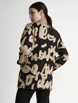 Saco acolchado con estampado abstracto en negro y beige, cuello redondo, cierre con botones a presión y bolsillos laterales. Incluye cinturón ancho de cuero negro con hebilla rectangular.