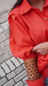 Camisa de lino color naranja, con mangas largas abuchonadas, cuello camisero y cierre frontal con botones. Presenta un diseño único con detalle calado en los puños.