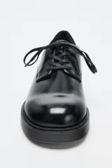 Zapato tipo blucher de estilo clásico con cierre mediante cordones. Presenta un acabado en punta redonda y suela con plataforma.