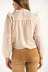 Blusa de color arena con diseño de volados en los hombros, detalle de fruncido en el pecho y mangas largas con puños elásticos.