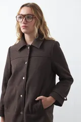 Tapado corto de paño color marrón, con diseño recto, cuello camisero y cierre frontal con broches metálicos. Cuenta con bolsillos frontales.