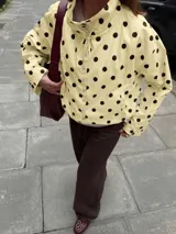 Chaqueta ligera de color amarillo con estampado de lunares negros, cuello alto, mangas largas anchas y cordón ajustable en el dobladillo inferior.