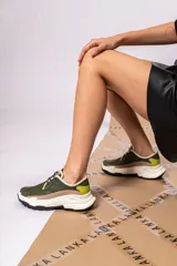 Championes urbanos de cuero verde con textura reptil, detalles en beige y amarillo, cordones negros y suela chunky blanca con base negra.