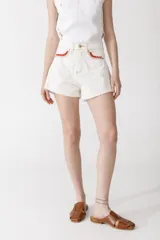 Short de denim color blanco roto, tiro alto, con terminación deshilachada en el ruedo. Presenta detalles de crochet en color rojo en los bordes de los bolsillos delanteros.