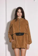 Buzo de pana color óxido, con diseño oversize, cuello alto con cierre frontal, bolsillo delantero tipo canguro con solapa negra y logo bordado, puños elásticos y ruedo ajustable con cordón.