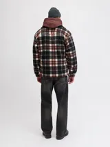 Sobrecamisa de textura tipo teddy con estampado de cuadros en tonos marrón, negro y crema. Presenta cuello camisero, cierre frontal de botones, bolsillos en el pecho y puños abotonados, con un corte relajado.