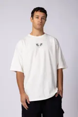 Remera de corte oversize color blanco hueso, con cuello redondo y estampa pequeña centrada en el pecho que presenta dos figuras de caballos alados.