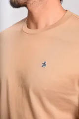Remera de manga corta con cuello redondo, confeccionada en algodón de color beige. Presenta un pequeño logo bordado de un pingüino en el pecho.