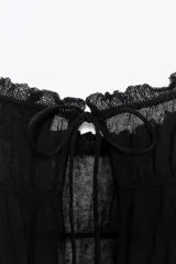 Top de manga larga negro, de tejido de punto semitransparente con efecto fruncido horizontal. Presenta cuello redondo con borde festoneado y cierre frontal con lazos finos.