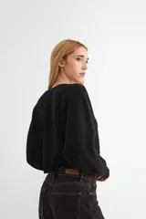 Sweater de punto negro, de corte holgado y diseño cropped, con cuello redondo y mangas largas.