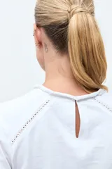 Remera blanca de manga tres cuartos con detalles de bordado calado en el frente y en los hombros, con cuello redondo y puños elásticos.