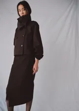 Chaqueta marrón de corte recto y diseño crop, confeccionada en mezcla de algodón y poliamida con forro interior de poliéster. Presenta cuello alto tipo embudo, doble botonadura frontal, manga larga y dos bolsillos laterales.