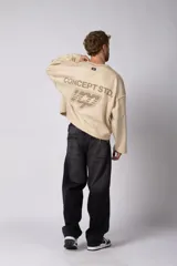 Buzo de cuello redondo confeccionado en tejido rústico con bordes al corte y costuras expuestas. Presenta un diseño boxy con estampado frontal y es reversible, permitiendo su uso por ambos lados.