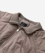 Campera bomber masculina de poliamida, con cuello, puños y ruedo de tejido elástico. Presenta cierre frontal con cremallera, dos bolsillos laterales con solapa y botón, y un pequeño bolsillo con cierre en una de las mangas.
