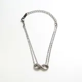 Collar de doble cadena fina de acero color plateado con un dije central en forma de símbolo de infinito. La cadena tiene un extensor con eslabones más grandes.
