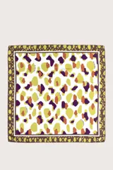 Pañuelo cuadrado de tejido ligero con estampado abstracto de manchas en tonos amarillo, morado y tierra sobre fondo blanco, con borde decorativo en tono marrón.