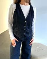 Chaleco de jean azul con broches metálicos y detalle de hebilla en la espalda.