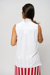 Camisa blanca sin mangas con cuello mao adornado con un delicado volado y cierre frontal con botones.