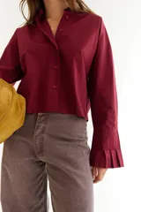 Camisa de corte boxy en color blanco, con cuello clásico, cierre frontal de botones y mangas largas con puños estructurados con tablas. Presenta costuras a contratono y detalle de frunce en la espalda.