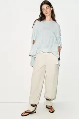 Top de cuello redondo color celeste con textura fruncida, mangas tipo capa y bajo asimétrico.