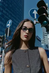 Chaleco jaspeado en tonos grises, con cuello redondo y sin mangas. Presenta cierre frontal con botones dorados y un cinturón fino negro con hebilla dorada.