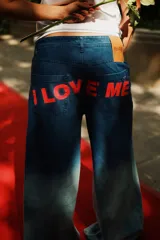 Jean de tiro medio, corte oversize y pierna ancha, confeccionado en denim 100% algodón con lavado degradé azul oscuro a claro. Presenta un estampado grande en color rojo en los bolsillos traseros con la frase "I LOVE ME". Tiene badana de PU color camel con logo grabado.