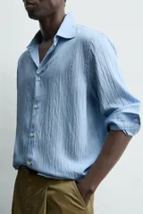 Camisa de corte relajado confeccionada en tejido fluido con mezcla de viscosa, color celeste. Presenta cuello solapa, manga larga con puños abotonados y cierre frontal de botones.