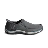 Zapatos tipo mocasín Skechers Slip-ins de la línea Relaxed Fit, color gris oscuro. Presentan una parte superior de lona, paneles elásticos laterales y un panel de talón moldeado con diseño texturizado. Incluyen suela con amortiguación y plantilla Air-Cooled Memory Foam.