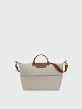 Bolso de viaje Longchamp modelo Le Pliage Original, de diseño ampliable, confeccionado en nylon negro con detalles en cuero marrón en las asas y solapa frontal con cierre de botón a presión. Incluye correa ajustable y extraíble.