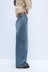 Jeans de tiro medio con diseño baggy barrel, confeccionados en denim color beige con efecto lavado. Presentan cinco bolsillos, costuras laterales torcidas y cierre frontal con cremallera y botón metálico.