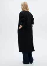 Abrigo largo de lana italiana Manteco, diseño oversize con cuello de solapa, cierre frontal de botones y cinturón desmontable. Presenta mangas largas con hebillas decorativas en los puños, dos bolsillos laterales y abertura posterior en el bajo.