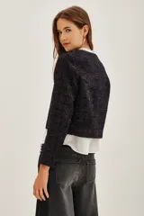 Saco corto de textura tweed en color azul oscuro con destellos metalizados. Presenta cierre frontal mediante tres trabas de cuero sintético con botones tipo toggle, cuello redondo y mangas largas.