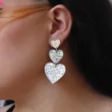 Aros colgantes con tres dijes de corazones holográficos de diferentes tamaños. Los corazones están unidos por argollas plateadas.