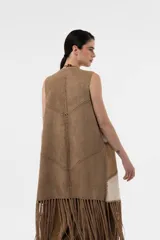 Chaleco largo de gamuza sin mangas con diseño de paneles en bloques de color beige y marrón, costuras decorativas visibles y flecos largos en el ruedo.