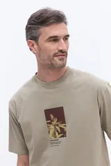 Remera de manga corta color beige, con cuello redondo y estampa gráfica central con motivos botánicos y texto.