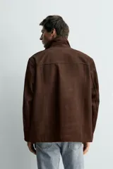 Cazadora de piel en color marrón, con corte relajado, cuello con solapas de muesca, cierre frontal con botones y bolsillos de plastrón en la parte delantera.