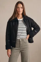 Campera tipo gamulán de corte oversize, color negro, con interior y detalles en cuello y puños de corderito sintético. Presenta cierre frontal y correas decorativas en el cuello.