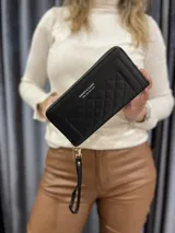 Billetera negra con diseño matelassé y cierre perimetral. Incluye correa de muñeca desmontable y logo estampado en el frente.