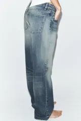 Jeans de tiro bajo y cinco bolsillos, con diseño de pierna ancha y larga. Presenta roturas y desgastes sutiles en la parte delantera. Cierre frontal con cremallera y botón metálico.