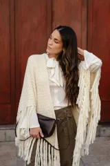 Poncho triangular de lana en color crudo, con diseño de tejido texturizado y terminaciones de flecos largos en todo el borde.