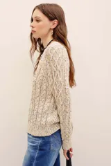 Sweater tejido de punto color beige con motas multicolor, cuello redondo y diseño de trenzas, de manga larga.