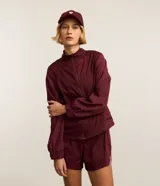 Campera rompevientos deportiva Get Over de color bordó, con cuello alto, cierre frontal con cremallera, mangas largas con puños ajustados y recortes con hilo reflectante.